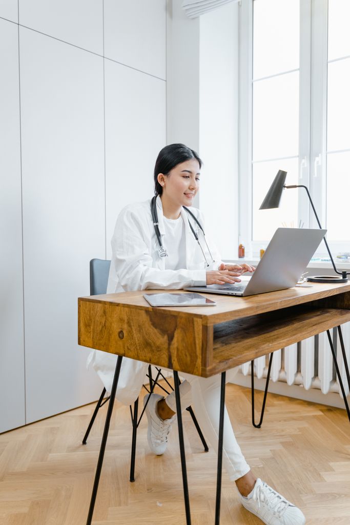 Female doctor using laptop for online consultation in a modern office setting.