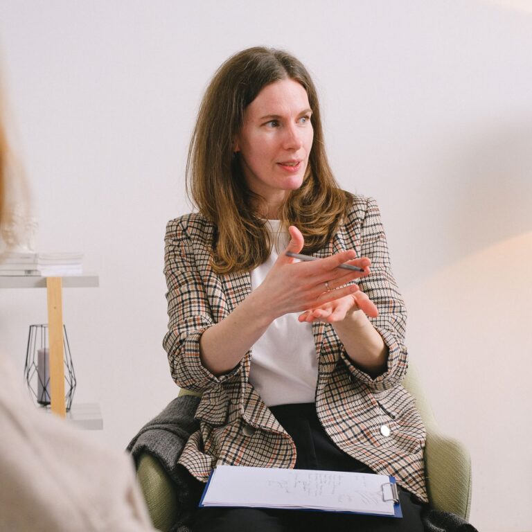 Pensive female psychologist in stylish clothes discussing problems with client in light room and looking away